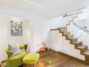 A modern interior with a staircase, a green armchair, a small table with a decorative item, and a wall with a geometric art piece. - Edgy & Designer Camden Town Apartment (Greater London)