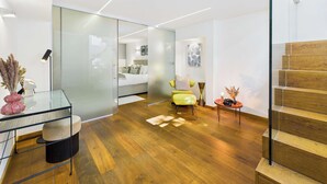 Un intérieur moderne avec une cloison en verre, un plancher en bois, un lit, une chaise jaune et un escalier.