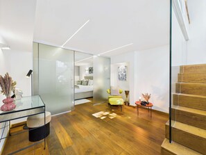 A modern interior with a glass partition, wooden flooring, a bed, a yellow chair, and a staircase.