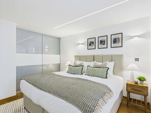 A modern bedroom with a large bed, a bedside table with a lamp, and a nightstand with a plant. - Edgy & Designer Camden Town Apartment (Greater London)