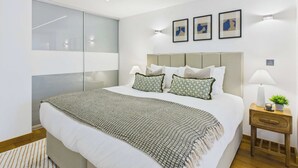 Une chambre moderne avec un grand lit, une table de chevet avec une lampe et une petite table de nuit agrémentée d’une plante.
