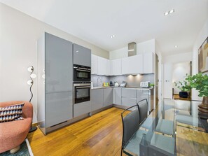 A modern kitchen with built-in appliances, a dining area with a glass table, and a red sofa. - Edgy & Designer Camden Town Apartment (Greater London)