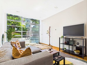 Una sala de estar moderna con un ventanal grande, un sofá, una mesa de centro y un televisor sobre un mueble negro.