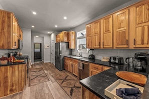 A modern kitchen with wooden cabinets, a black countertop, and a stainless steel refrigerator.