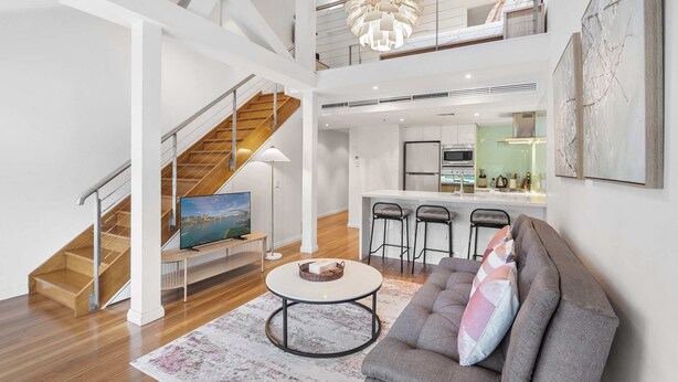 A spacious living area with a staircase, a dining area, and a kitchen. - Loft-Style Waterfront Apartment (Woolloomooloo)