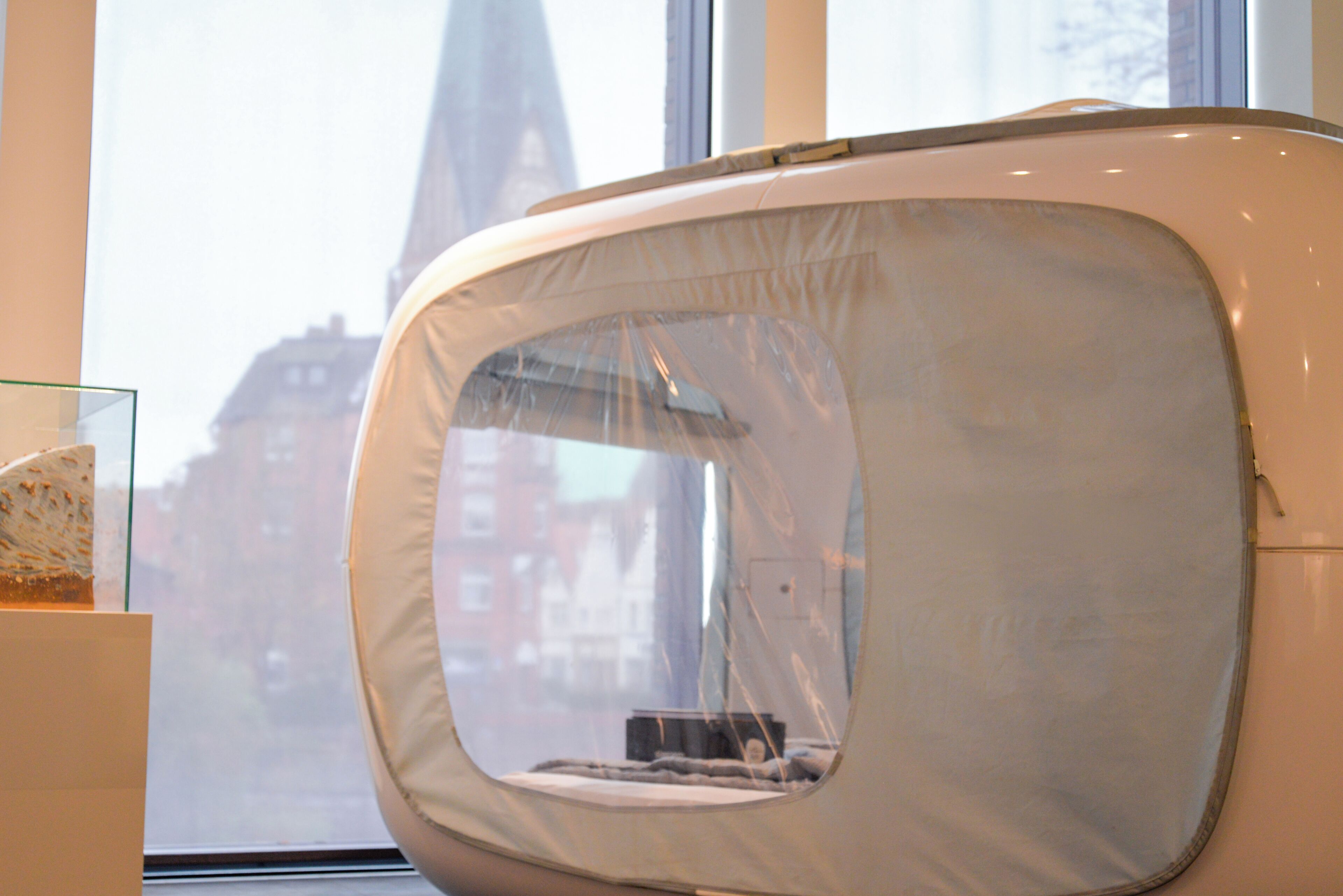 Ein modernes, gebogenes Bett mit Fenster, einer Glastausche und Blick auf Gebäude.