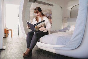 Una persona sentada en una cama en una habitación con una ventana, leyendo un libro.