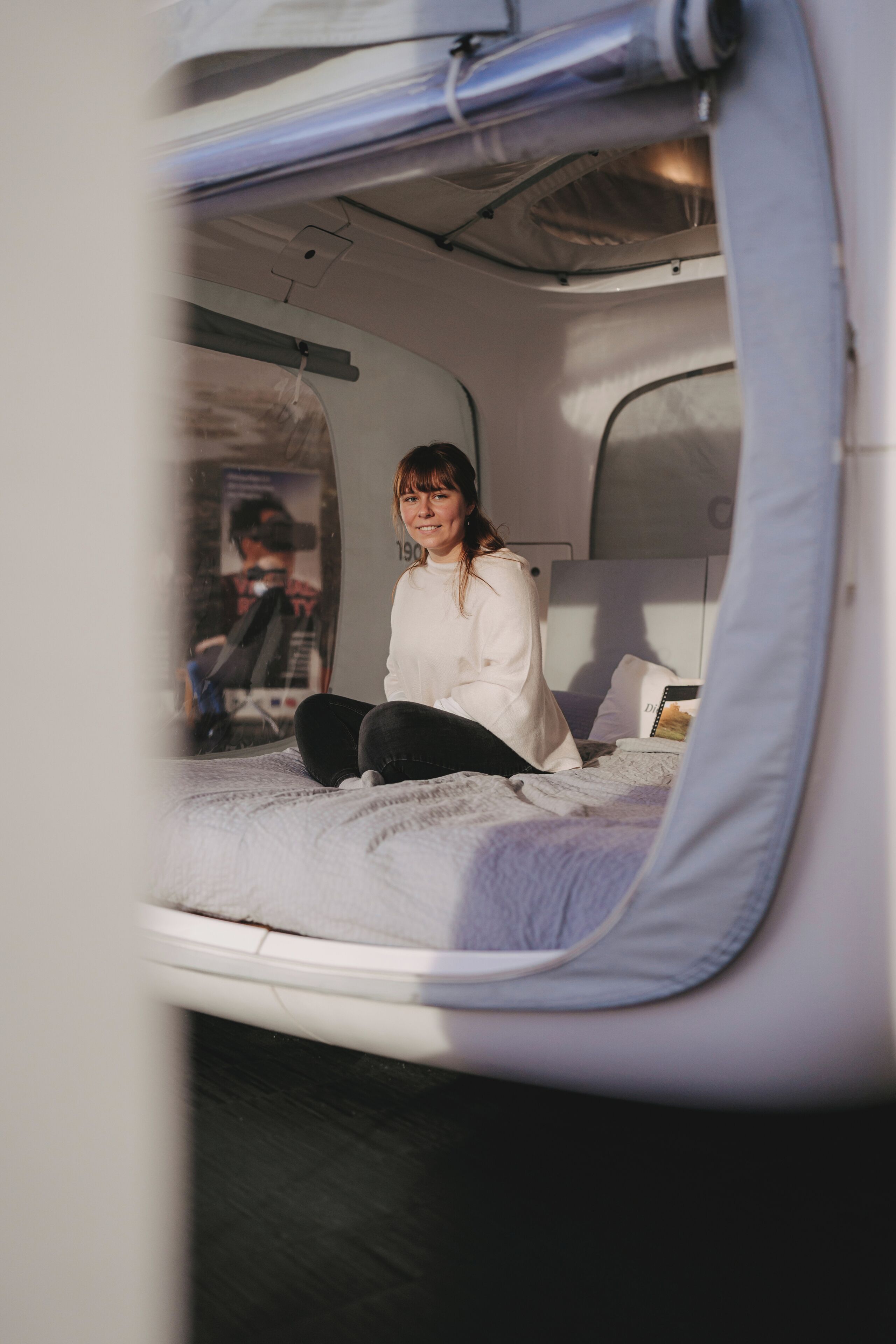 Eine Person sitzt auf einem Bett in einem Fahrzeug, mit Kopfstütze und Kissen.