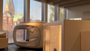 A modern interior with a circular seating area, a stone sculpture, and a view of a historic building through large windows. - Eine Nacht im Museum - LUNA Sleep Cube (Lueneburg)