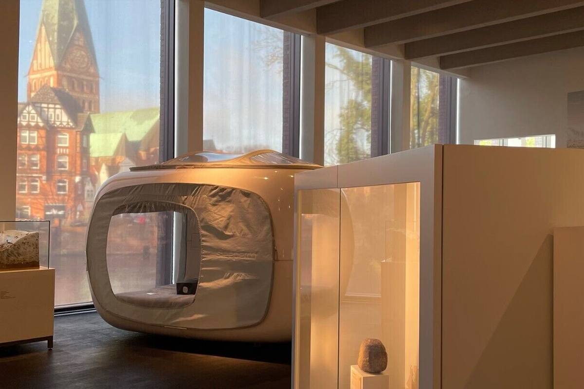 Ein modernes Interieur mit einer runden Sitzecke, einer Steinskulptur und Blick auf ein historisches Gebäude durch große Fenster.