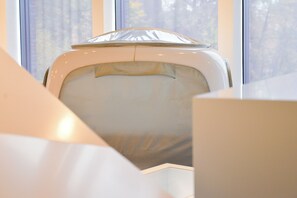 Una habitación con un ventanal grande, una silla blanca y una vista parcial de una cama.