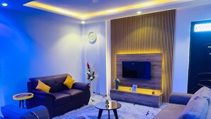 A modern living room with a sofa set, a coffee table, and a flat-screen TV mounted on a wooden wall. - Jac-Kuw Splendour Homes (Accra)