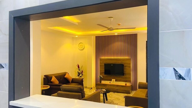 A modern living room with a sofa set, a coffee table, and a flat-screen TV mounted on a wooden panel wall. - Jac-Kuw Splendour Homes (Accra)