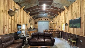 A rustic cabin interior with wooden walls, a leather sofa, a dining table, and a kitchen area. - Charming 3-bedroom cabin in Autaugaville with AC and Hangout Building (Autaugaville)