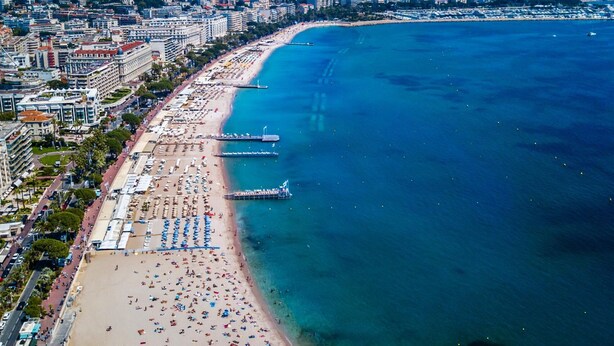 An aerial view of a coastal city with a long beach lined with rows of umbrellas and sunbeds, a pier extending into the sea, and high-rise buildings along the shore. - TOWNHOUSE 5 MN WALK FROM CANNES CROISETTE (Cannes)
