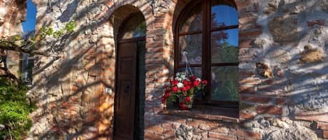 Experience the charm of a traditional stone building with a wooden door and a window adorned with a hanging flower basket.