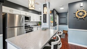 Una cocina moderna con electrodomésticos de acero inoxidable, encimera de granito, iluminación colgante y decoración de temática náutica.