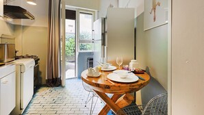 A compact kitchen with a dining area, a refrigerator, a stove, and a window with curtains. - Loquat House by Rentbeat (Roma)
