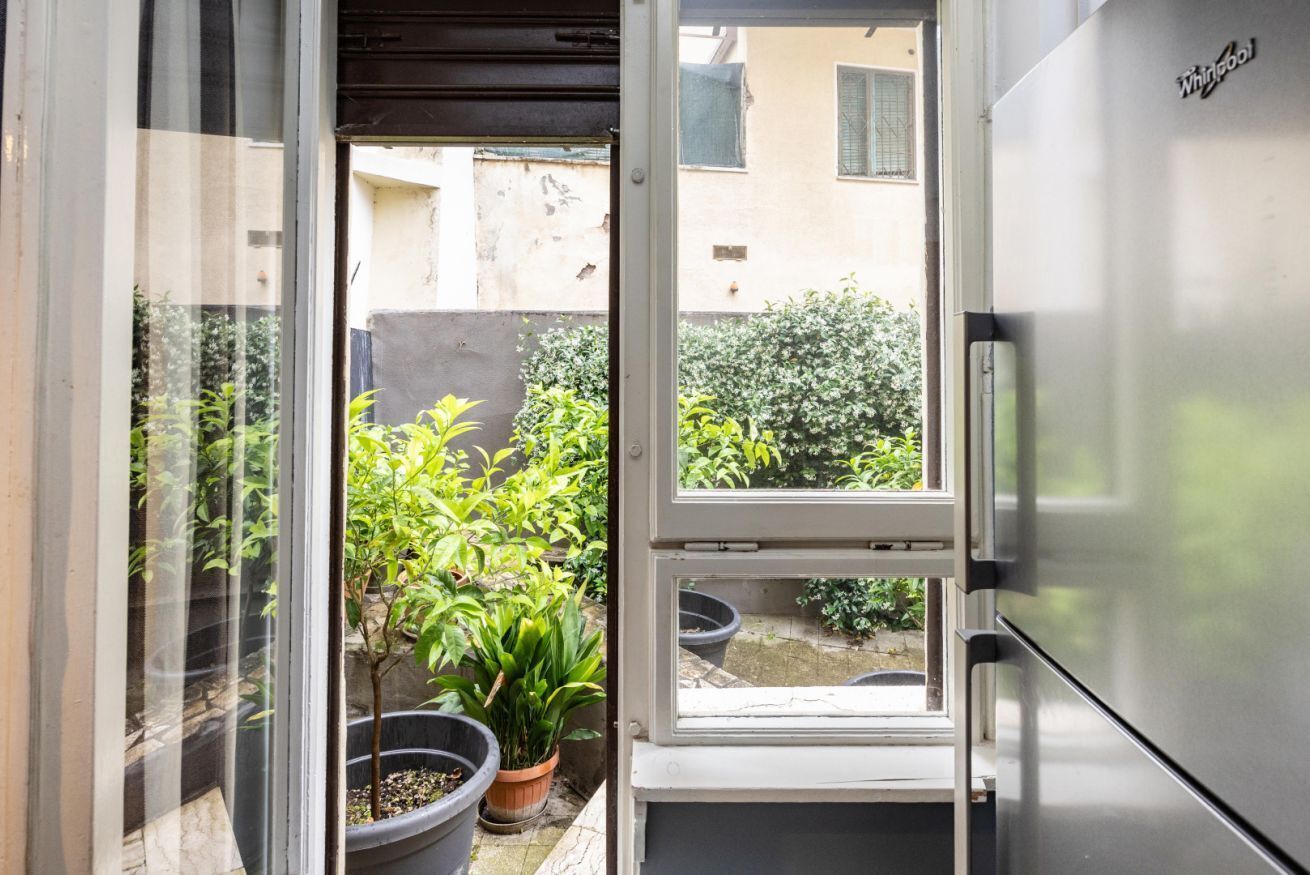 A kitchen with a refrigerator, a window, and potted plants.