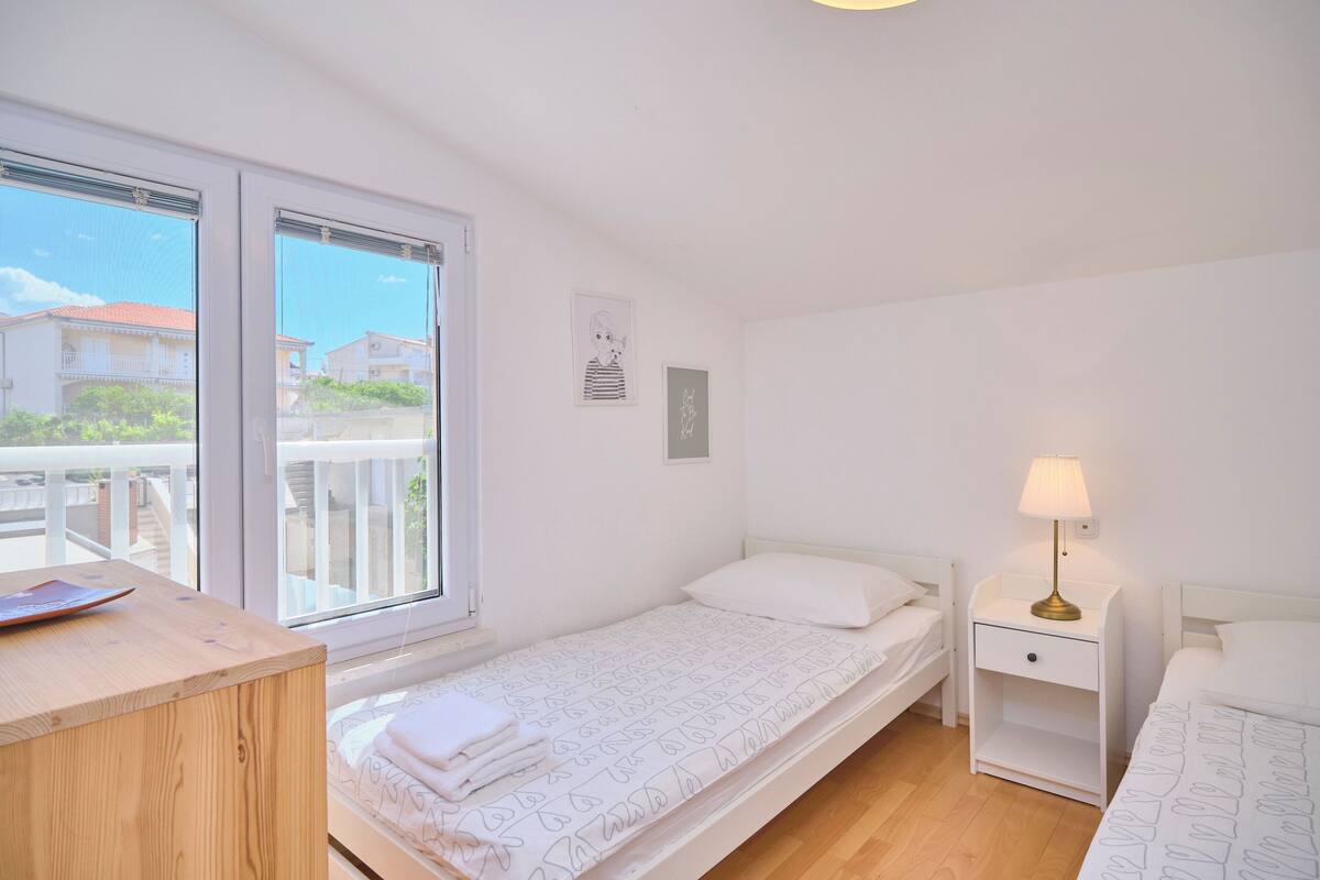 A small, bright room with a single bed, a nightstand with a lamp, and a wooden desk.