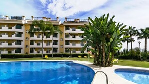 A swimming pool with a clear blue water, surrounded by a well-maintained lawn and palm trees. - Aloha Banús Sea Views by Lica Homes (Marbella)