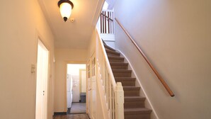 A hallway with a wooden staircase, a light fixture, and a door leading to another room. - Rural Home Near the Soesterduinen (Soest)