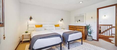 Un dormitorio con dos camas, un aparador, un espejo y una escalera.