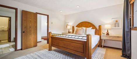 Un dormitorio con cama de madera, una mesita de noche, un espejo y una puerta que da a otra habitación.