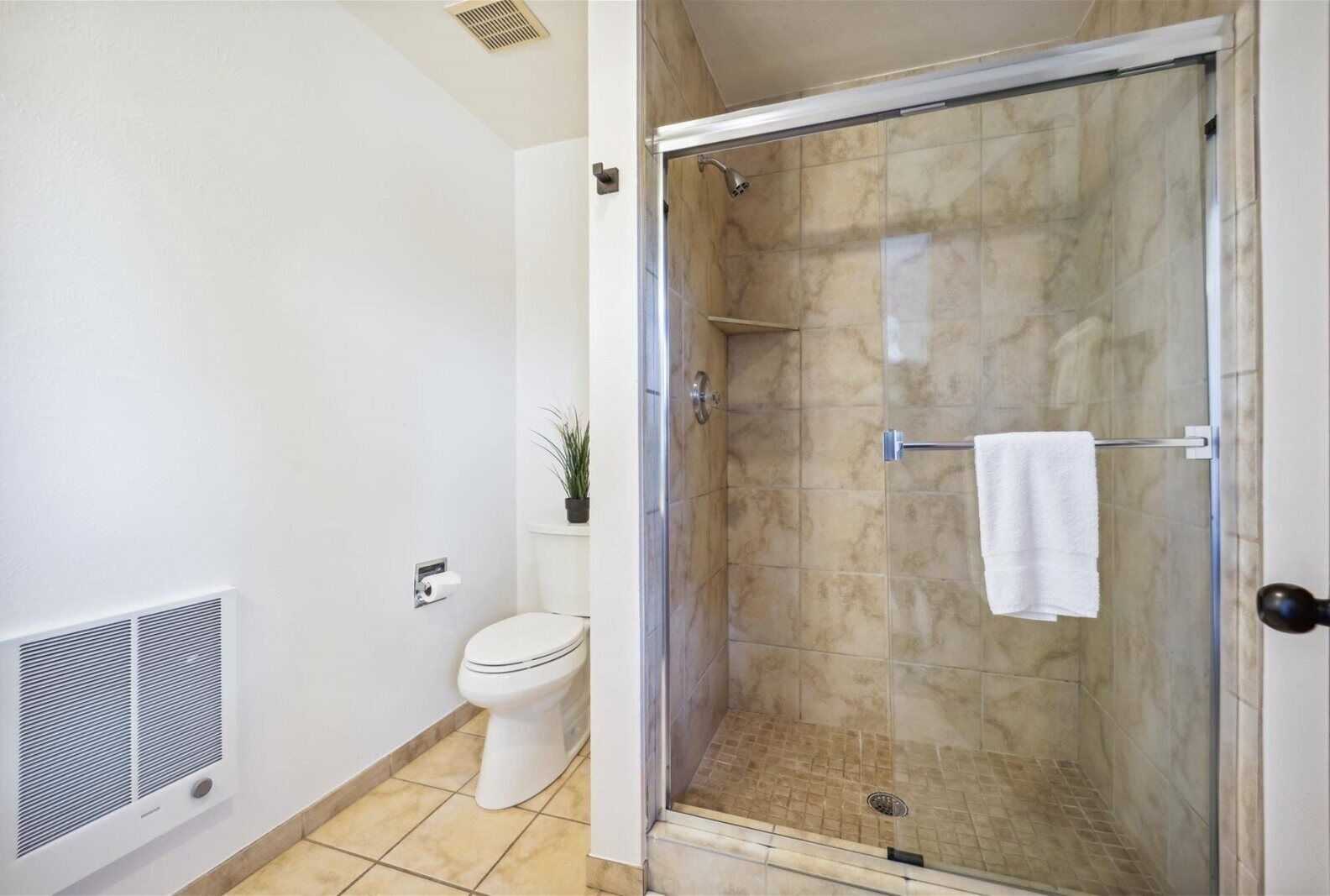 A bathroom with a glass-enclosed shower, a toilet, and a vent.