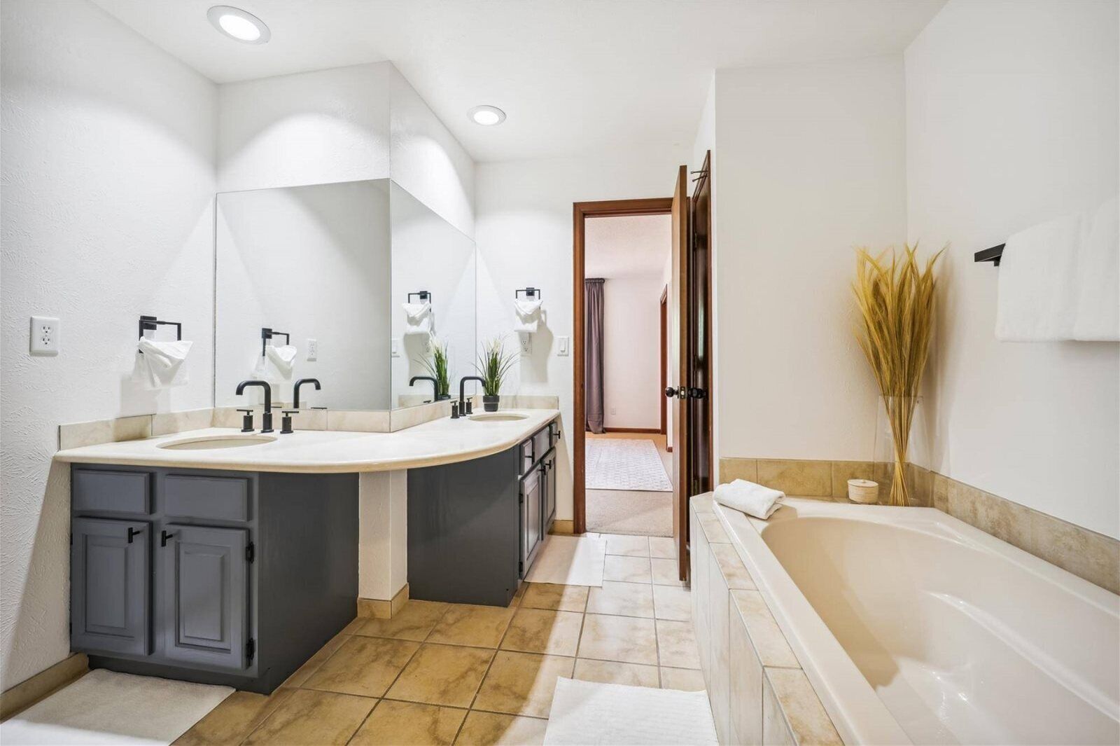 Uma casa de banho moderna com lavatório duplo, um espelho grande, uma banheira e uma porta que dá para outro espaço.
