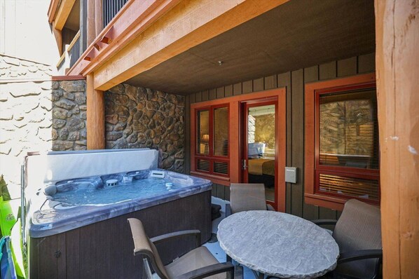 Un jacuzzi con sillas y una mesa frente a un edificio de paredes de piedra y puertas de madera.