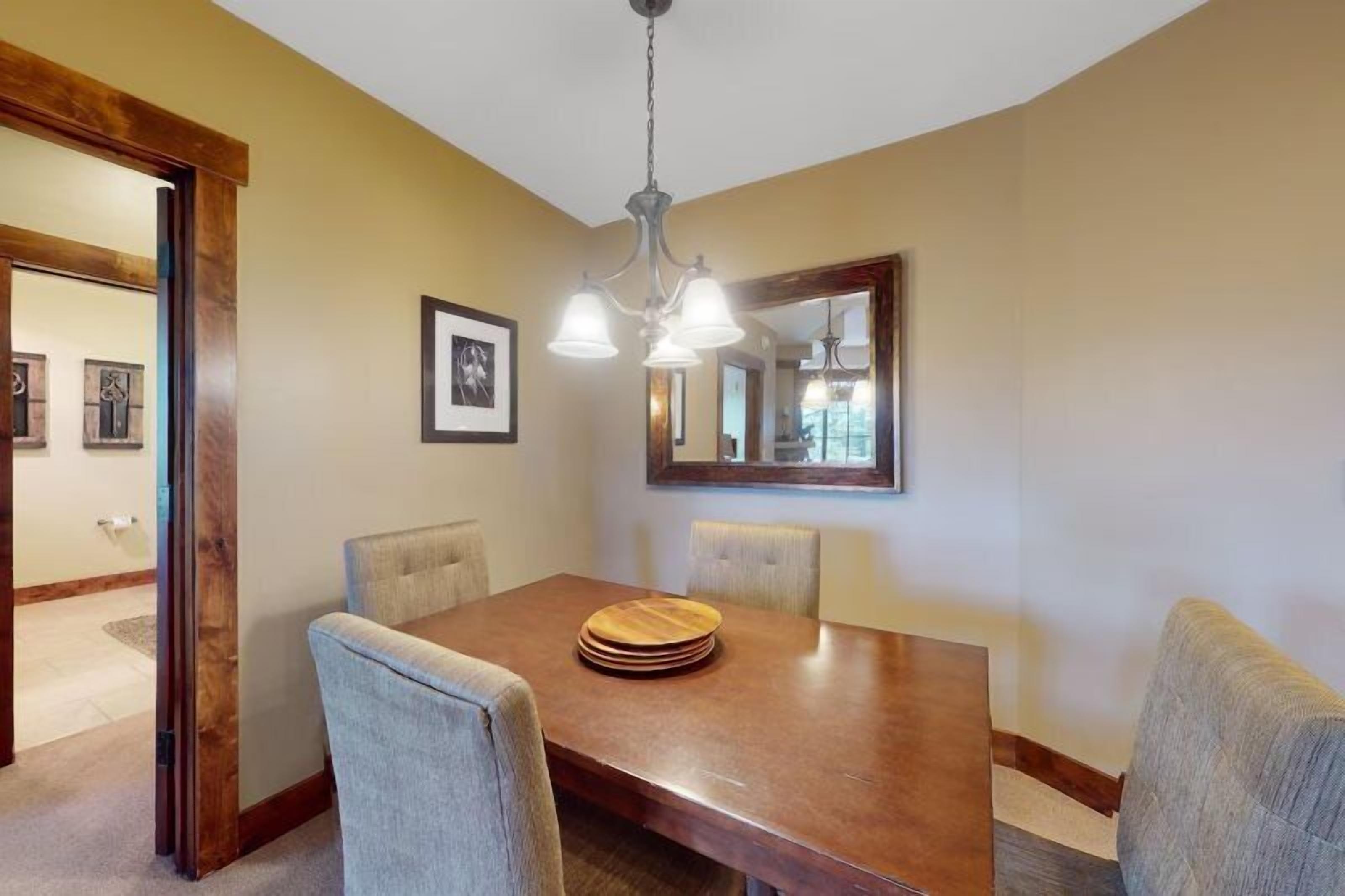 A dining room with a wooden table, four chairs, a chandelier, and framed pictures on the walls.