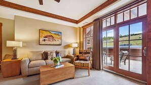A spacious living room with a sofa, a coffee table, and a chair. There is a painting on the wall and a large sliding glass door leading to an outdoor area. - Ski-in/ski-out One Ski Hill Place 2 Bedroom Luxury Condo (Breckenridge)