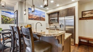 A kitchen with a central island, dark wooden cabinets, stainless steel appliances, and pendant lighting. - Luxury One Ski Hill 2 Bedroom Ski-in/out Condo at Peak 8 (Breckenridge)