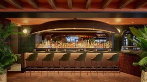 Un espace bar doté d’un plafond en bois aux lignes courbes, d’une variété de bouteilles d’alcool et de cinq chaises modernes.