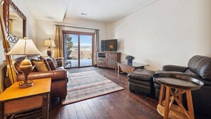 Un salon comprenant un canapé, une table basse, un téléviseur et une porte-fenêtre coulissante donnant sur un balcon.