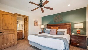 A bedroom with a large bed, wooden headboard, two bedside tables with lamps, a ceiling fan, and a wooden door. - Ski-in/ski-out 2 Bedroom Condo at The Village at Breckenridge (Breckenridge)