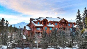 Un amplio lodge de madera con varios balcones, rodeado de árboles cubiertos de nieve y una montaña al fondo.