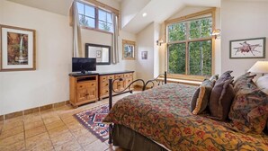 Een slaapkamer met een groot bed, een televisie, een kast en een raam met uitzicht op bomen.