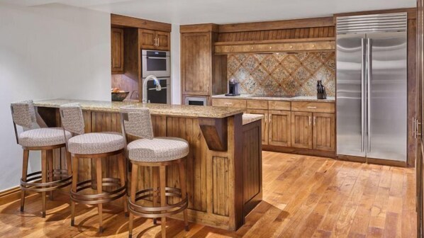 A kitchen with wooden cabinets, a stainless steel refrigerator, and a bar area with stools.