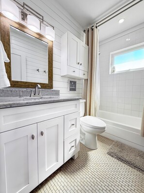 Een moderne badkamer met een witte wastafel, een grote spiegel, een badkuip en een toilet.