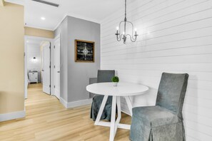 Een moderne eethoek met een ronde witte tafel, gestoffeerde grijze stoelen, een kleine potplant en wanddecoratie met een kompas thema.