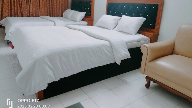 A hotel room with two beds, a chair, and a curtain. - HOTEL GOLDEN BIRD (Dhaka)