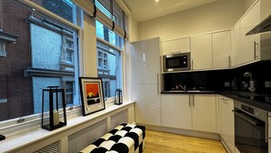 Cocina moderna con armarios blancos, microondas y estufa. En el alféizar de la ventana hay un cuadro con una puesta de sol.