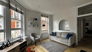 Una sala de estar moderna con un sofá gris, una mesita de centro redonda con flores, un sillón gris y una estantería.