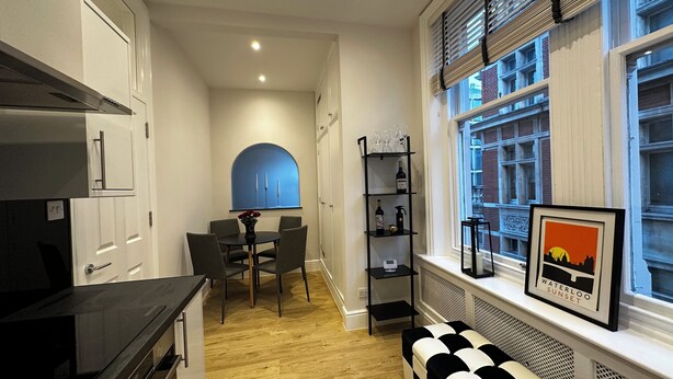 Una cocina moderna con comedor, un banco blanco y negro, y una estantería con copas y botellas de vino.