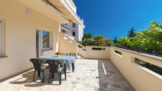 Un patio con una mesa y sillas, un pequeño jardín y un edificio con balcón.
