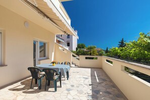 Eine Terrasse mit Tisch und Stühlen, ein kleiner Garten und ein Gebäude mit einem Balkon.
