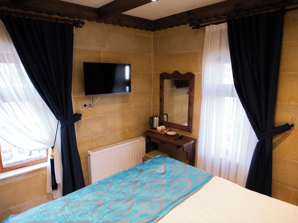 A room with a bed, a television mounted on the wall, a small table with a mirror, and curtains.
