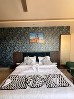 Hotellihuone, jossa on suuri sänky, pääty ja kuvioitu tapetti yhdellä seinällä.